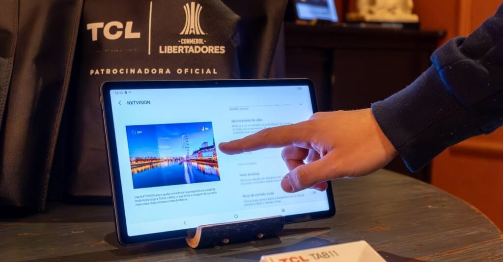 A hand interacts with a tablet display in a tech showroom featuring TCL products.